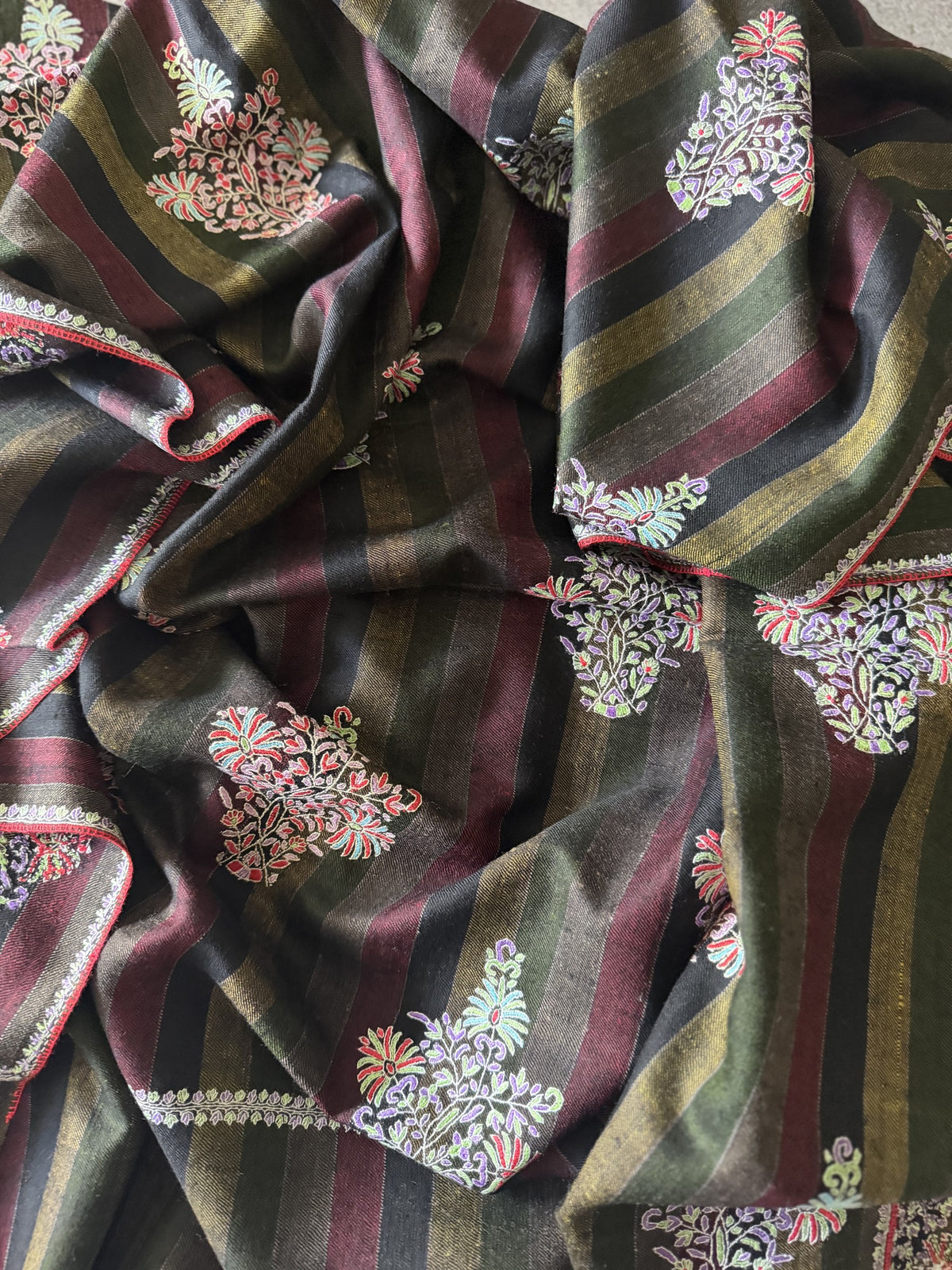 Close-up of coral, mint and lilac Sozni floral bouquets on charcoal, olive and wine striped pashmina