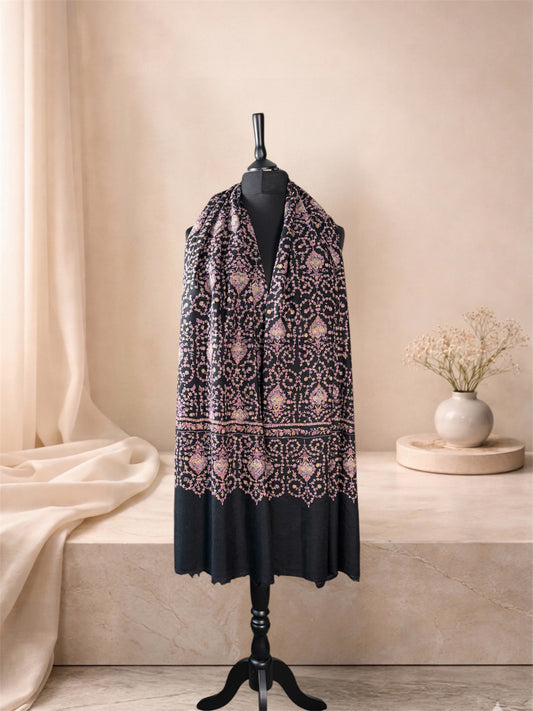 Black pashmina shawl with all-over rose and gold embroidery worn over the shoulders, front view