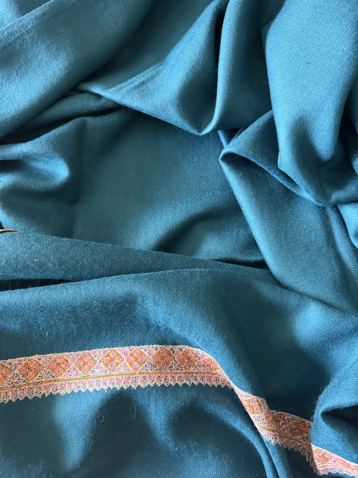Close-up of coral Sozni diamond border on teal blue pashmina