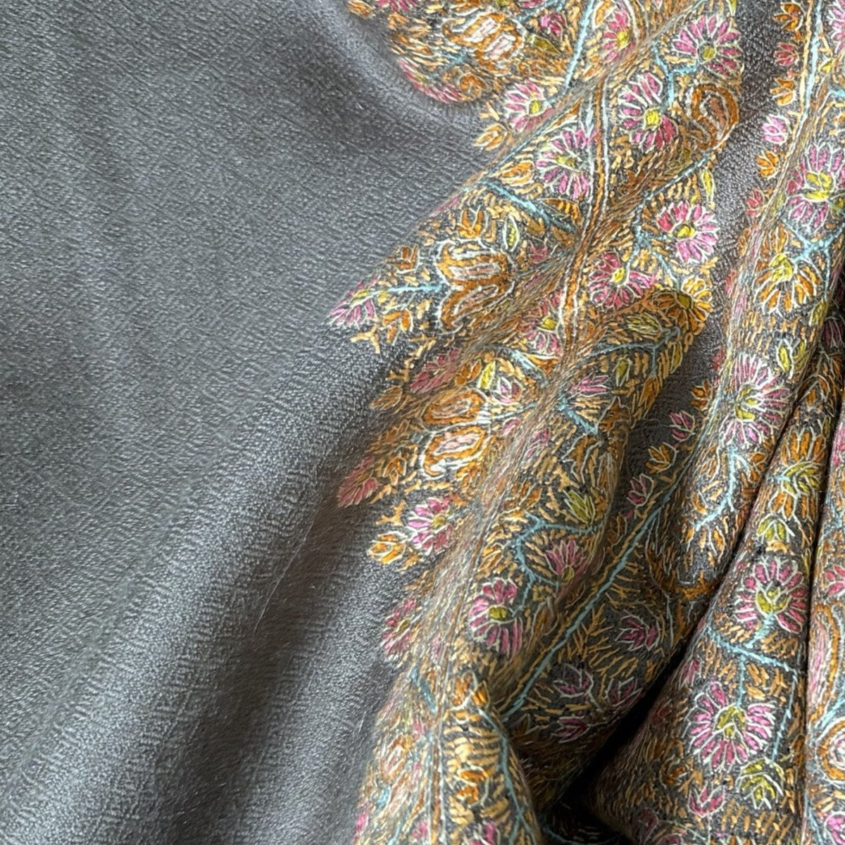 Close-up of grey Chashm-e-Bulbul (nightingale's eye) diamond weave pashmina beside gold, rose and aqua Sozni embroidery